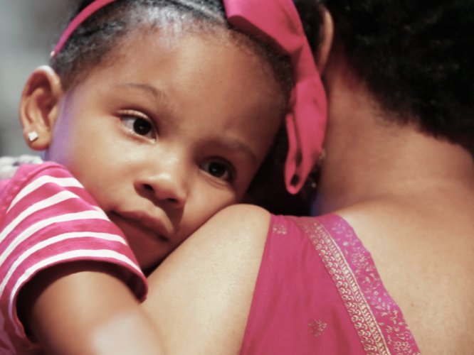 little girl wearing pink looks over the shoulder of woman holding her